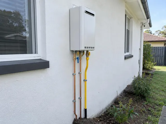 Wall-mounted hot water system with exposed pipes beside a house exterior in Bolwarra